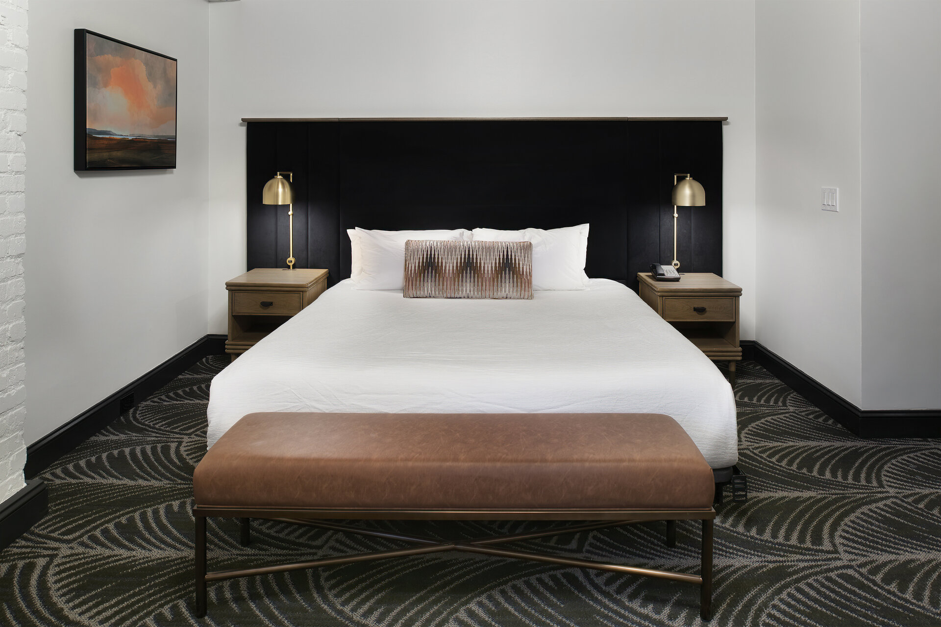 A hotel room with a large bed, brown bench, and wood nightstands