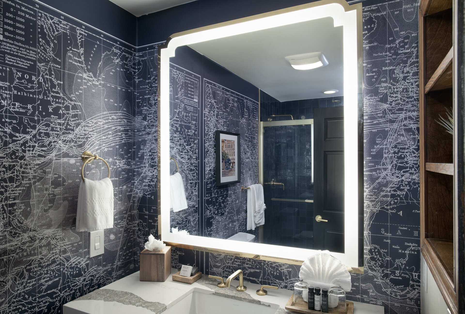 A bathroom with a large mirror, navy blue wallpaper, and gold fixtures.