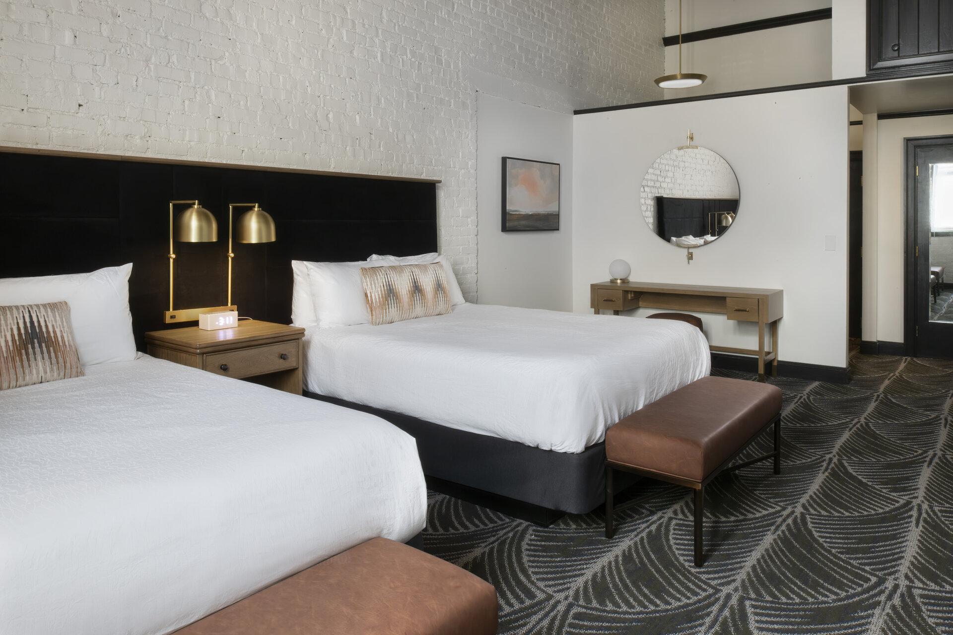 A hotel room with two beds, a nightstand, a desk, and a mirror.