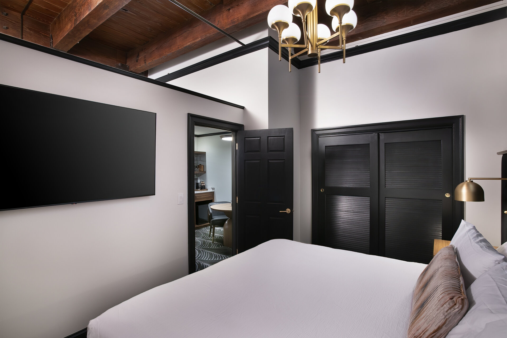 A hotel room with a king-sized bed, flat-screen TV, chandelier, and doorway to bathroom