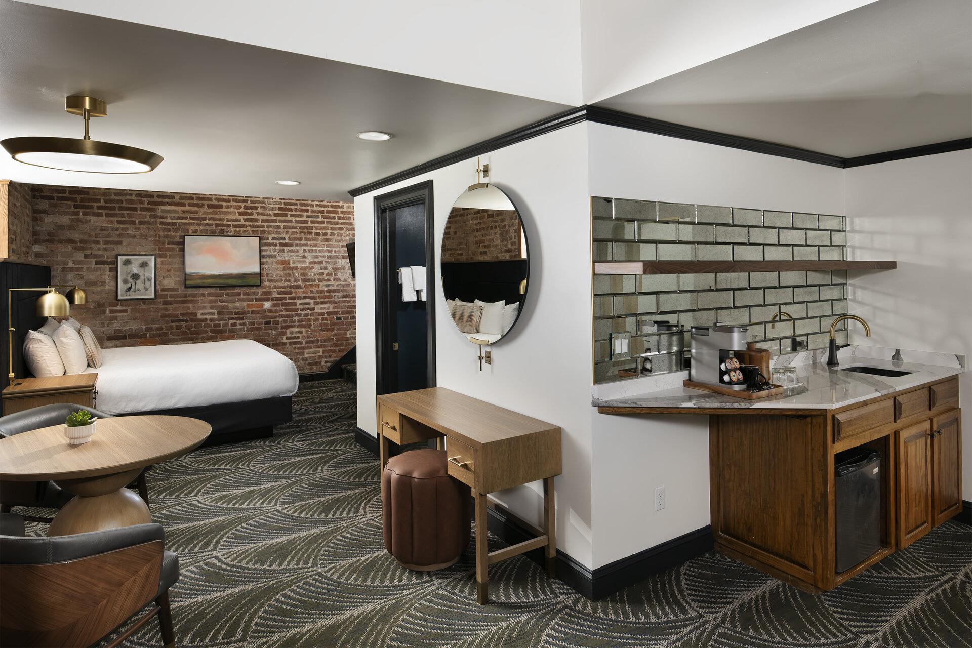 A hotel room with a kitchenette, dining table, desk, and bed