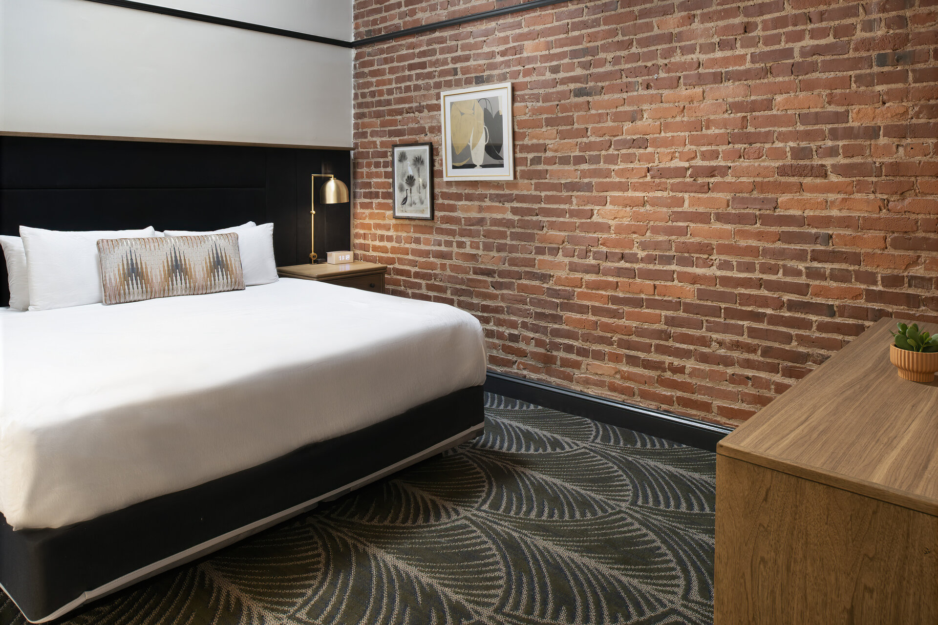 A hotel room with a bed, desk, and brick wall