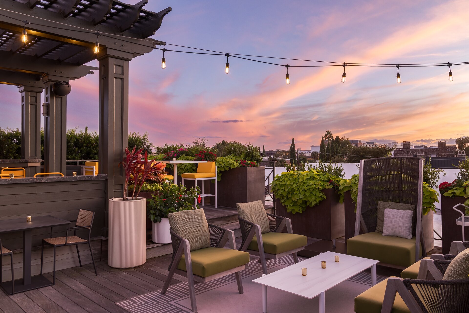 A rooftop patio with outdoor seating and a view of the city at sunset.